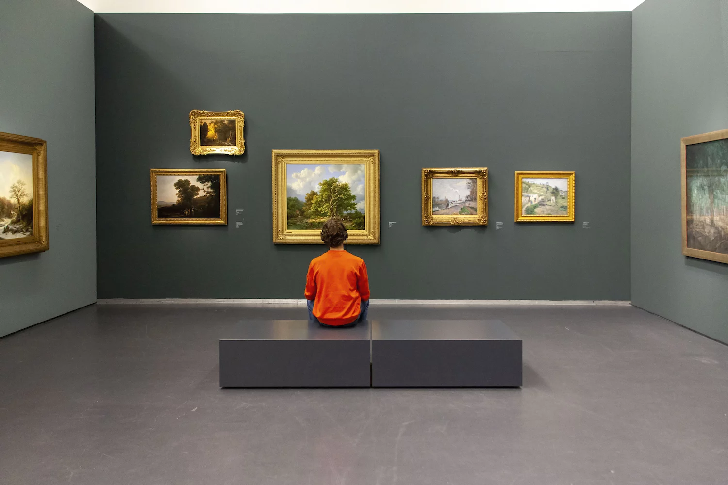 De bezoeker zit op een bankje in het museum. Voor hem hangen verschillende schilderijen en terwijl hij naar deze kunstwerken kijkt, luistert hij naar opgenomen perspectieven die daarover ingesproken zijn.