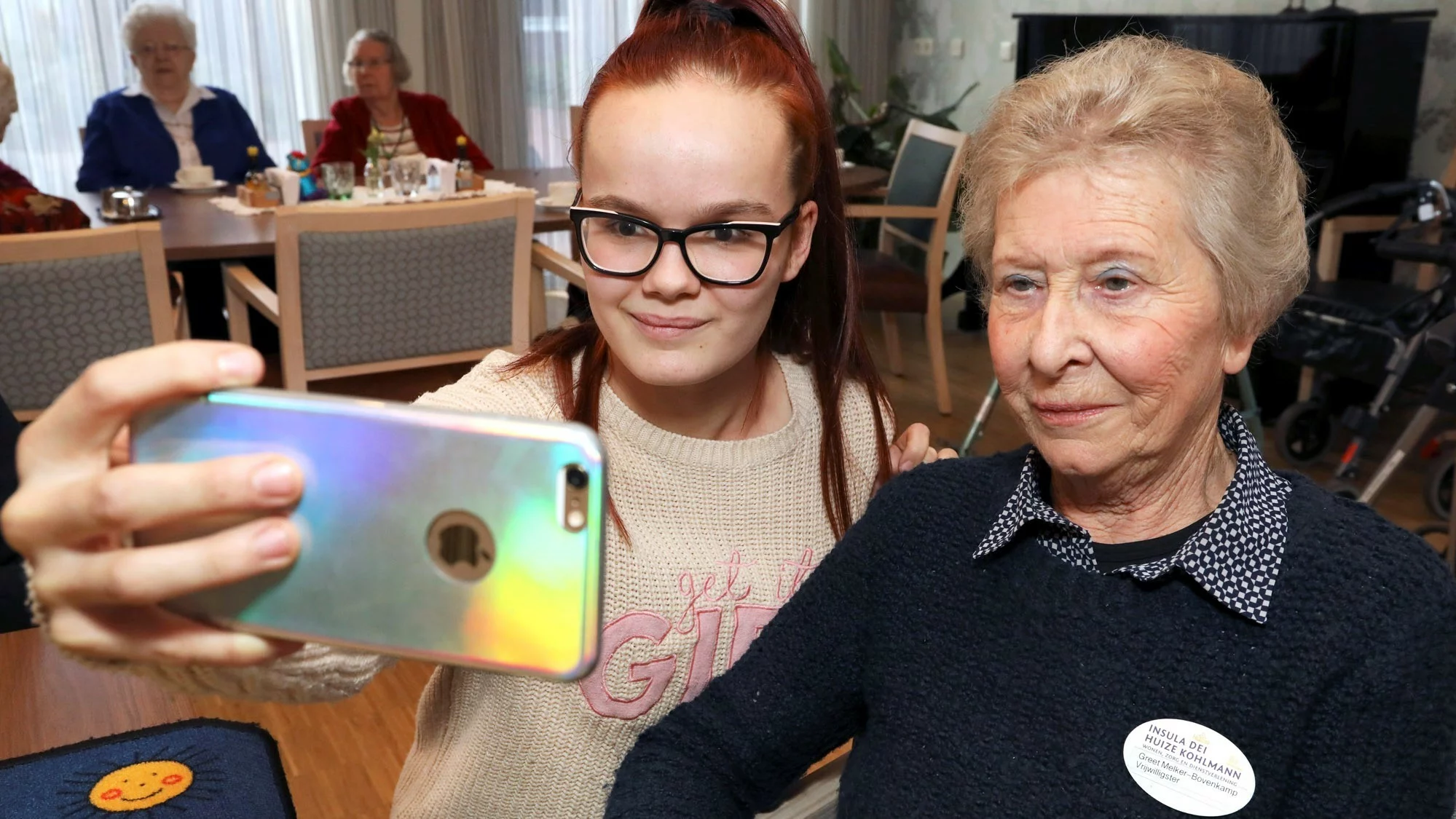 Een jongere neemt een selfie met een oma, ze zitten in een bejaardentehuis.