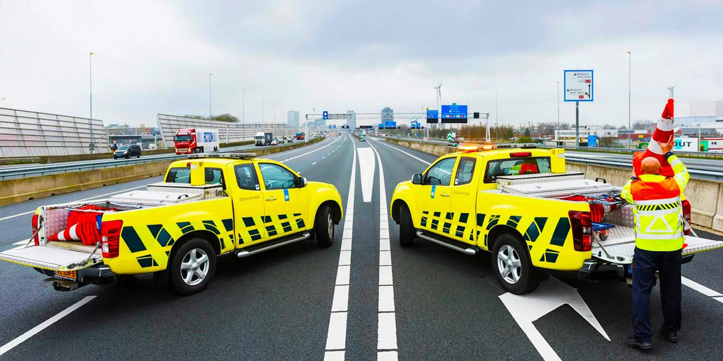 Twee auto’s van Rijkswaterstaat tijdens werkzaamheden op de snelweg, een medewerker zet in pion in de laadbak.