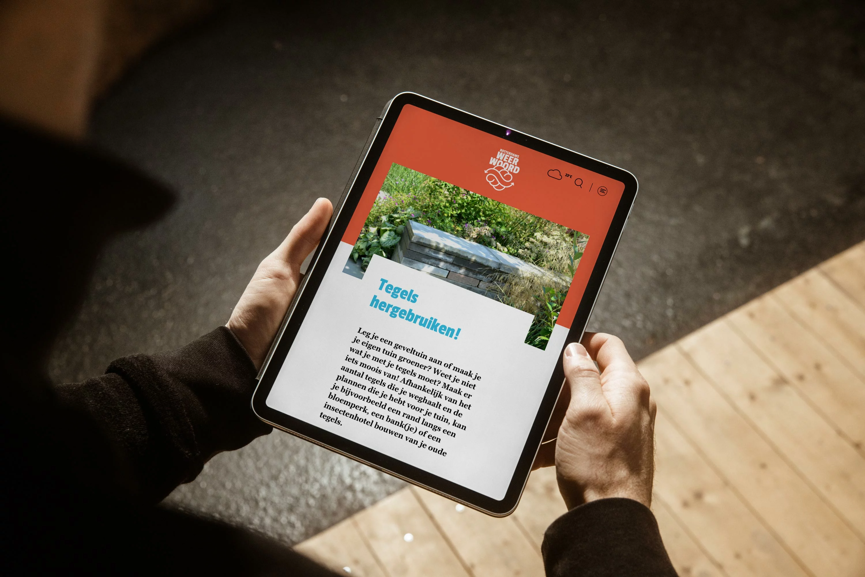 Iemand houdt een iPad vast met daarop de pagina van tegelwerken, hierop kunnen mensen tips vinden over wat ze met hun tegels uit de tuin kunnen doen. Van inspiratie tot een heel stappenplan.