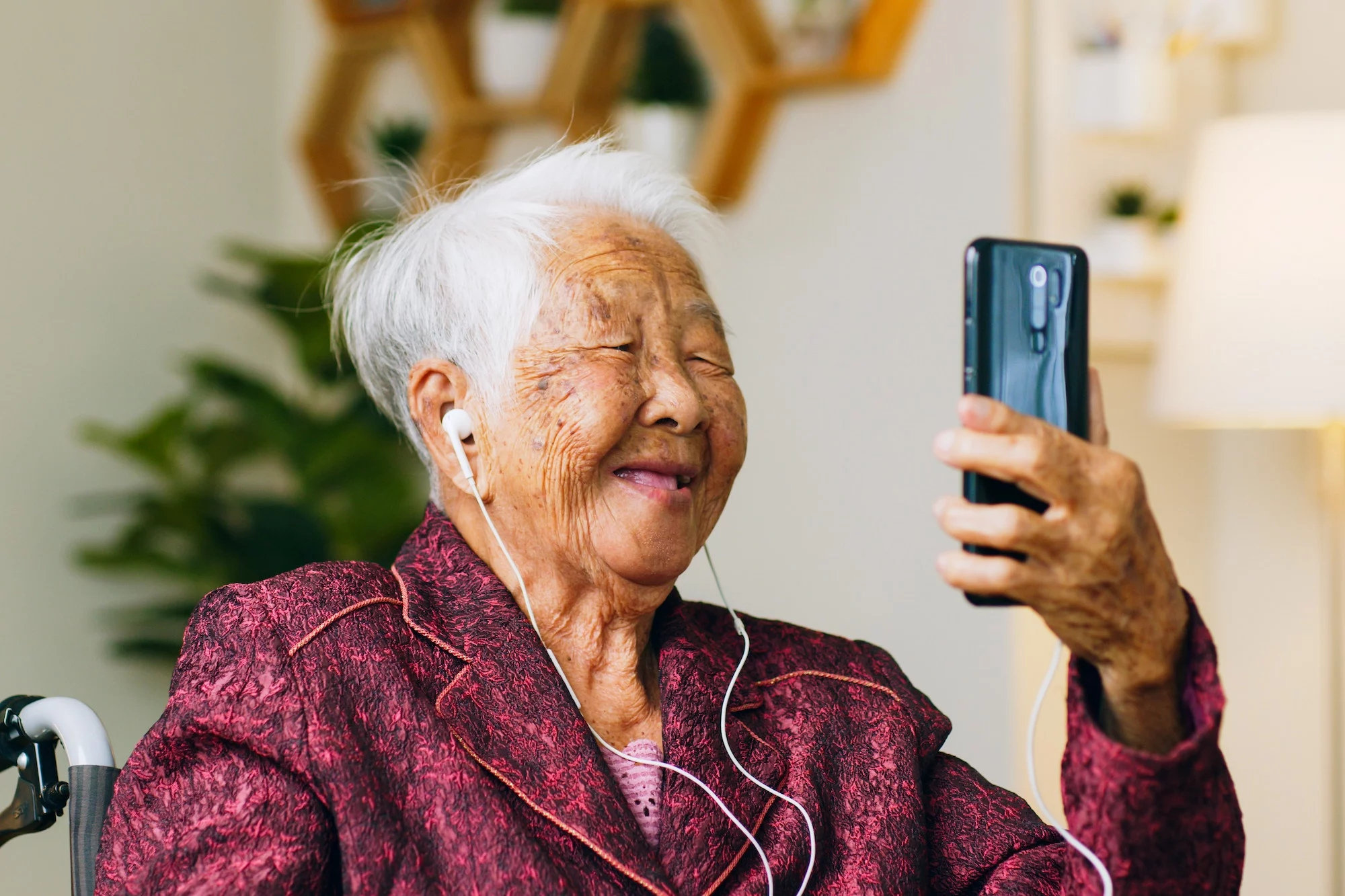 Oudere vrouw in rode jas met telefoon aan het bellen via oortjes.